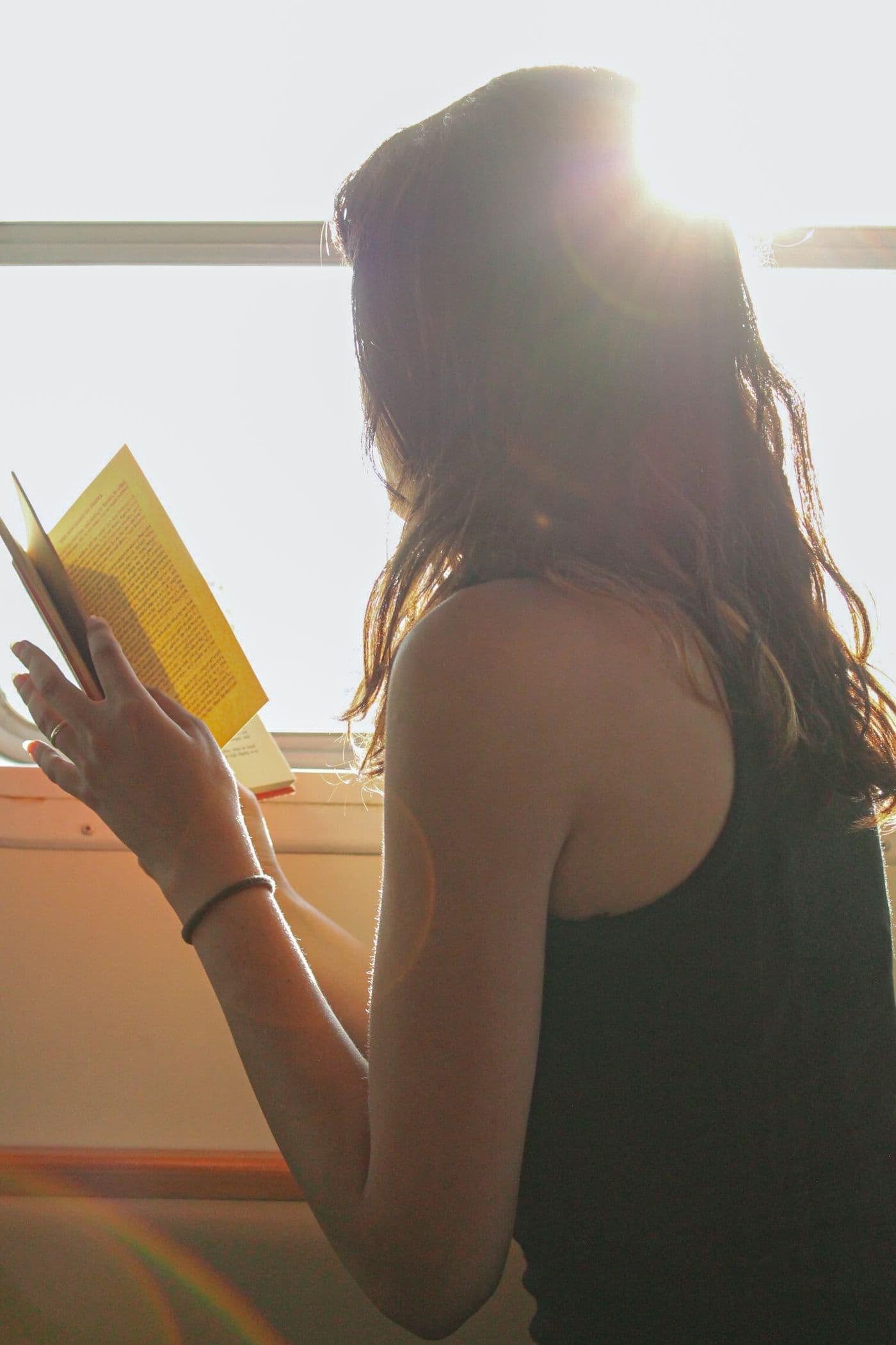 Una donna legge un libro vicino alla finestra, in controluce